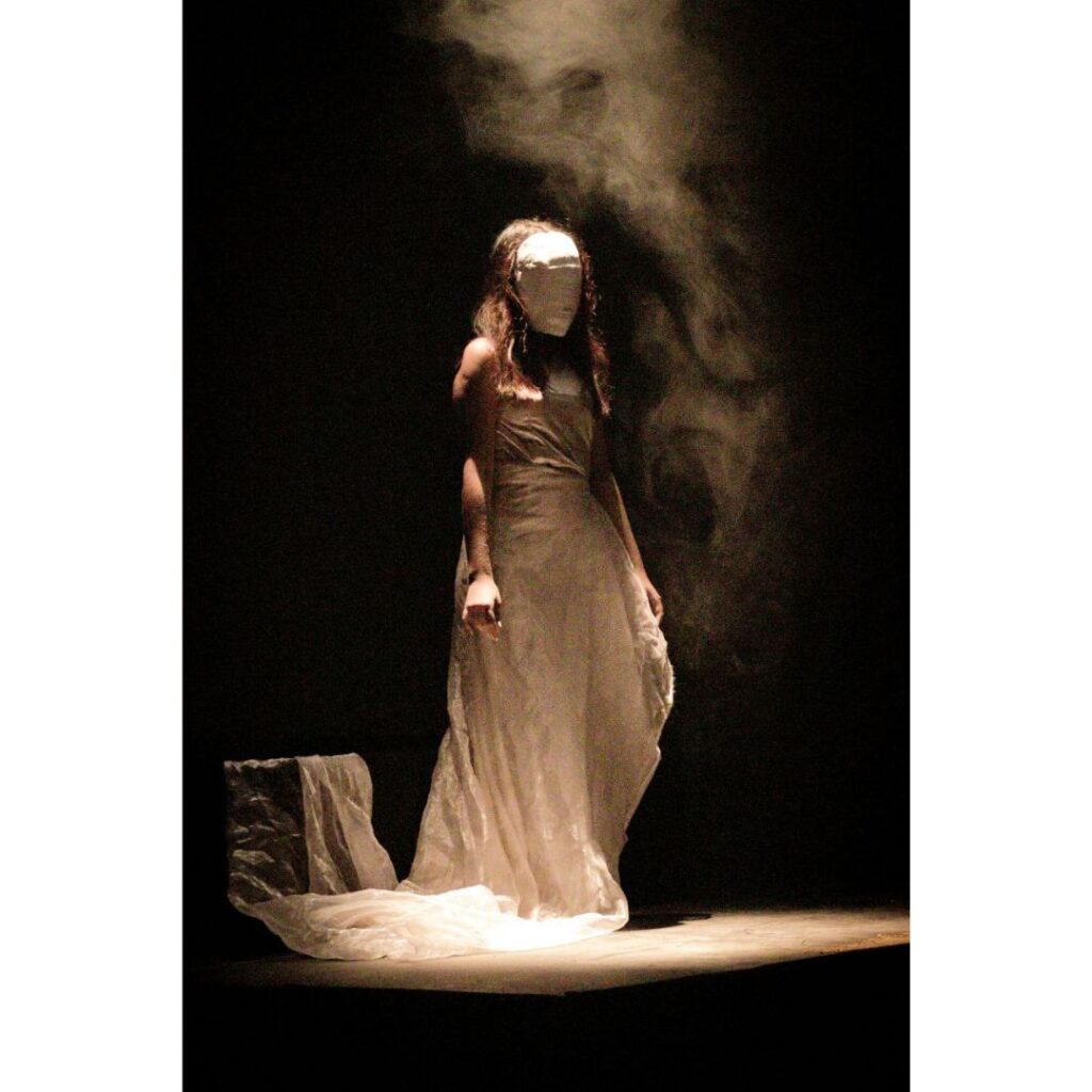 Fotografía de obra de teatro mujer con el rostro tapado y saliendo del humo 